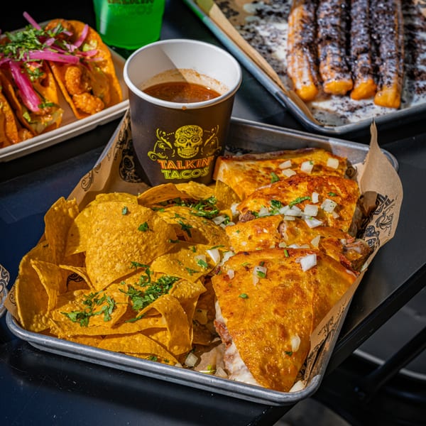 Talkin' Tacos birria tacos, tortilla chips, and a cup of consommé on a metal tray.