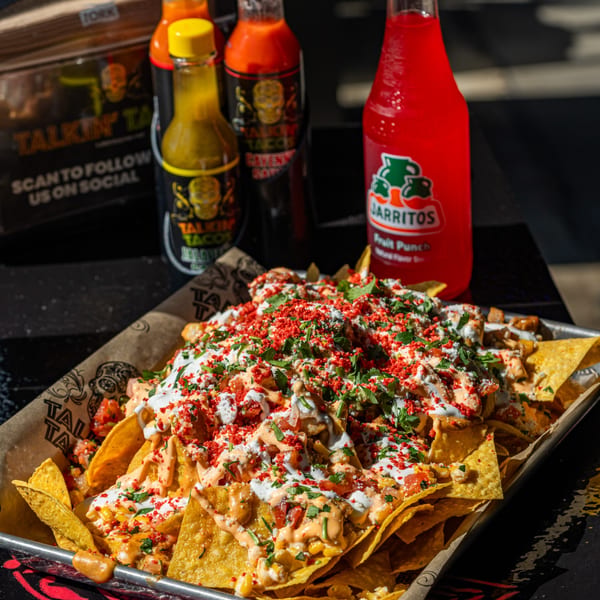 Talkin' Tacos nachos with red seasoning, cilantro, and sauces, alongside hot sauces and a Jarritos soda.