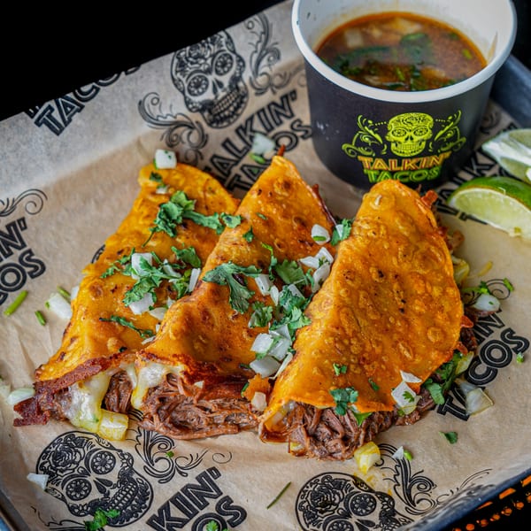 Three Talkin' Tacos birria tacos with melted cheese, cilantro, and onions, served with consommé and lime.