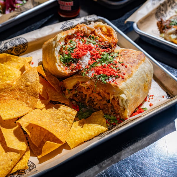 A large Talkin' Tacos burrito, cut in half, with chips on a metal tray.