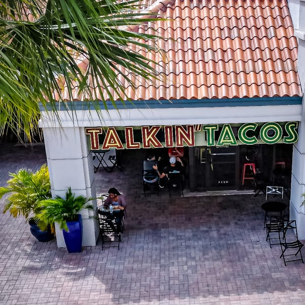 Overhead view of Talkin' Tacos restaurant entrance with a person dining outdoors and palm trees.