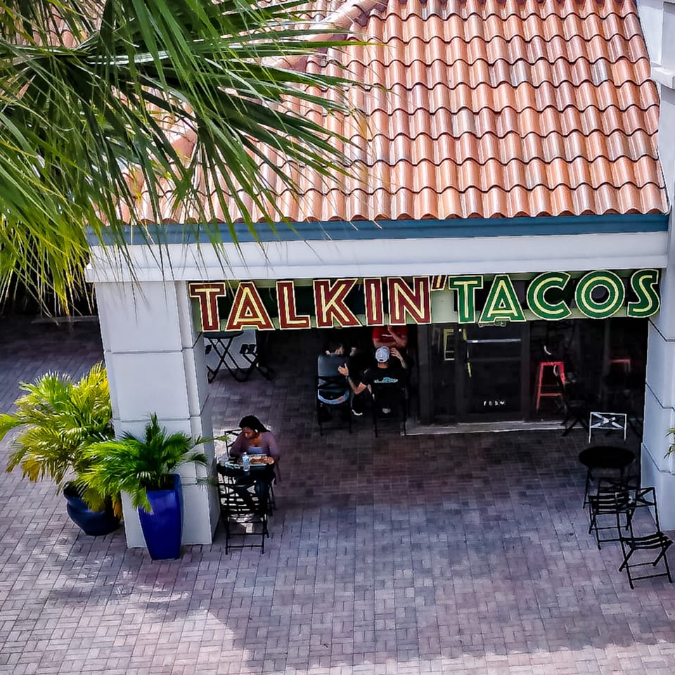 Overhead view of Talkin' Tacos restaurant entrance with a person dining outdoors and palm trees.
