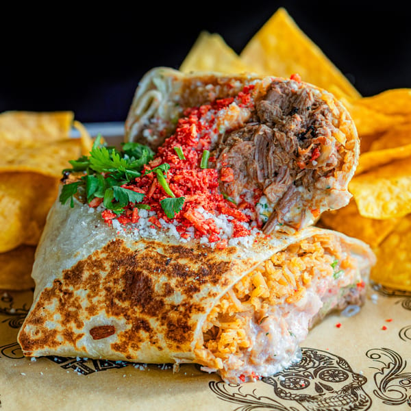 A large, cut open Talkin' Tacos burrito with meat, rice, red flakes, and cilantro, served with tortilla chips.