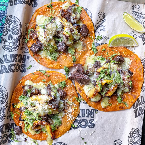 Three Talkin' Tacos with meat, cheese, cilantro, and lime wedges on branded paper.