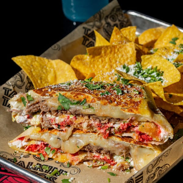 A Talkin' Tacos quesadilla with melted cheese, meat, and red chips, served with tortilla chips.