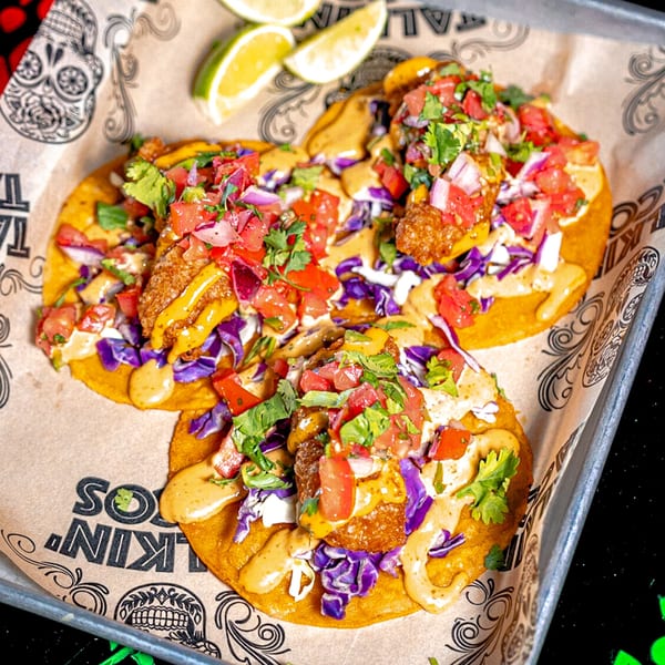 Three Talkin' Tacos with fried fish, purple cabbage, pico de gallo, and sauce on branded paper.