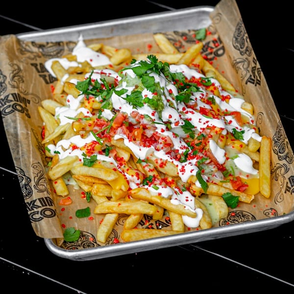 Talkin' Tacos loaded fries with white sauce, red sprinkles, guacamole, and cilantro on a tray.