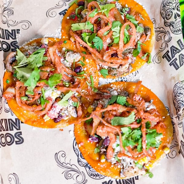 Three Talkin' Tacos with crispy onions, cilantro, and cotija cheese on branded paper.