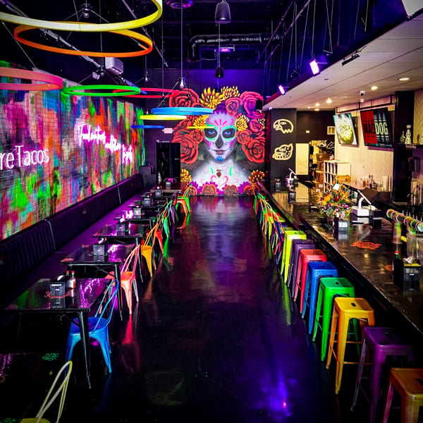 Vibrant Talkin' Tacos interior with colorful chairs, neon lights, and a large Day of the Dead mural.