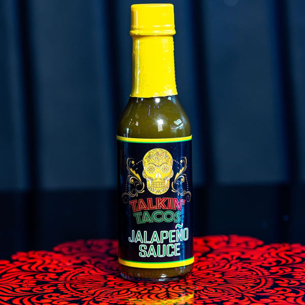 A bottle of Talkin' Tacos Jalapeño Sauce with a yellow cap and a sugar skull label.