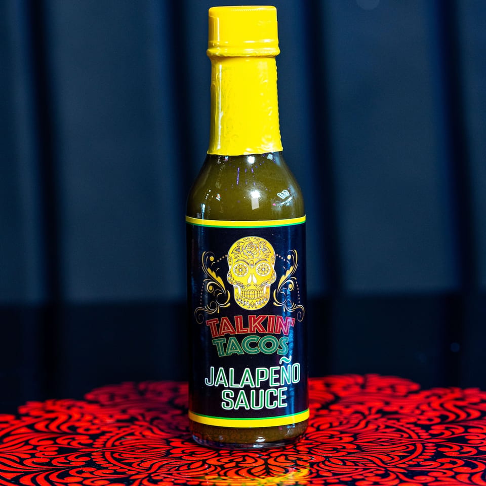 A bottle of Talkin' Tacos Jalapeño Sauce with a yellow cap and a sugar skull label.