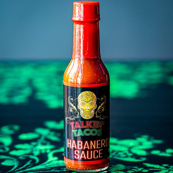 A bottle of Talkin' Tacos Habanero Sauce with a skull logo on a green and black surface.