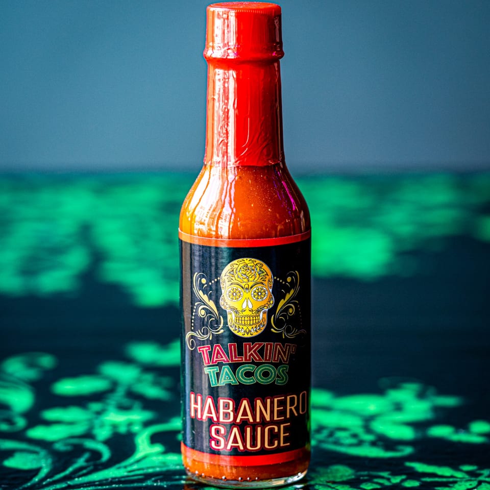 A bottle of Talkin' Tacos Habanero Sauce with a sugar skull label on a green patterned surface.