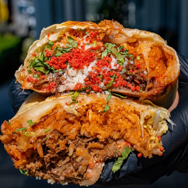 A large burrito from Talkin' Tacos, cut in half, revealing rice, meat, cheese, and red toppings.