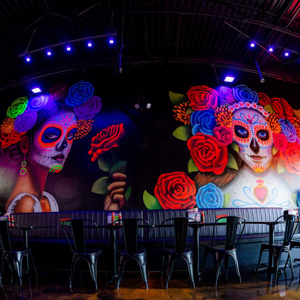 Talkin' Tacos restaurant interior with vibrant Day of the Dead murals and dark seating booths.