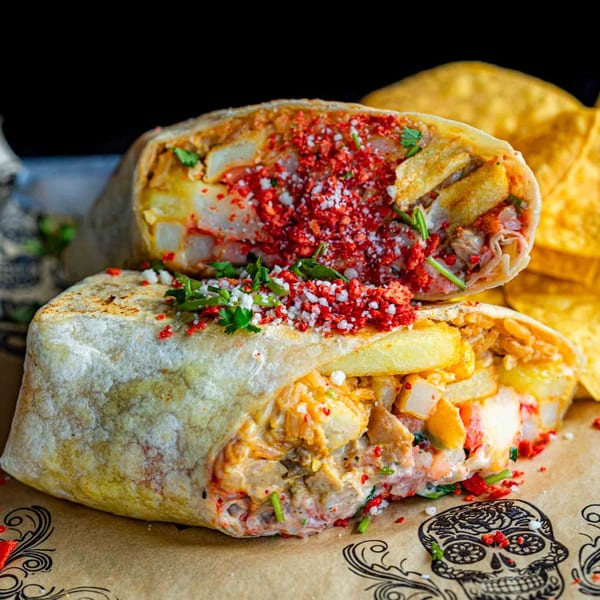 Two halves of a Talkin' Tacos burrito, filled with meat, fries, and red and white toppings.