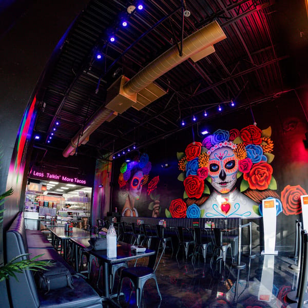 Interior of Talkin' Tacos restaurant with vibrant Day of the Dead murals and modern seating.