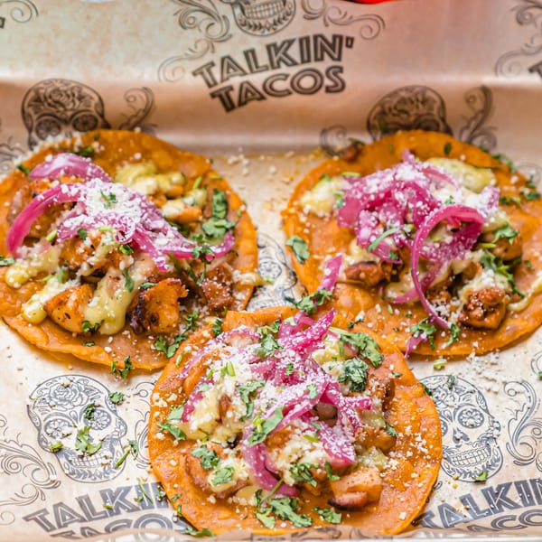 Three Talkin' Tacos with chicken, cheese, red onions, and cilantro on branded paper.