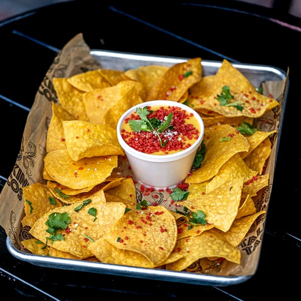 Talkin' Tacos' nachos with a cup of cheese dip, topped with red seasoning and cilantro.