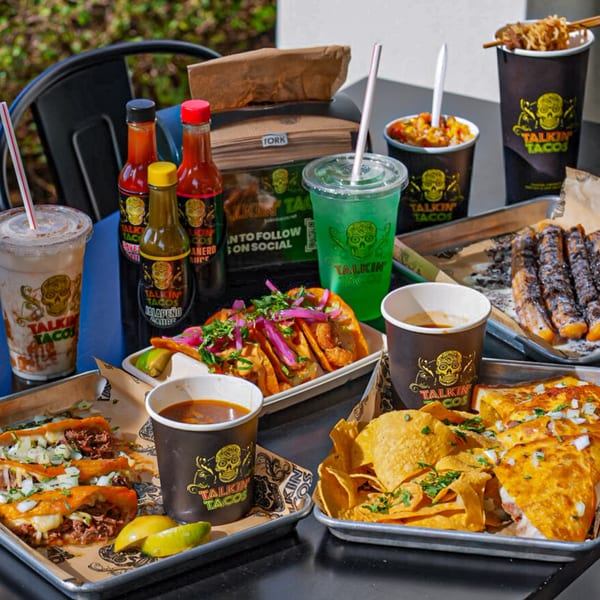 A table laden with various Talkin' Tacos dishes, drinks, and hot sauces.