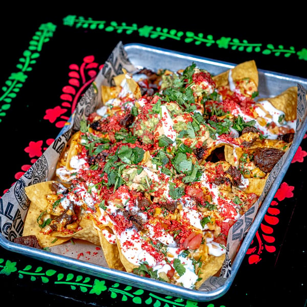 A tray of Talkin' Tacos nachos with meat, cheese, guacamole, sour cream, and red sprinkles.