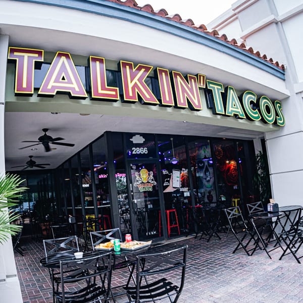 The Talkin' Tacos restaurant exterior with outdoor seating, food, and drinks on tables.