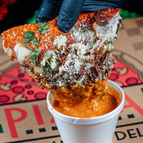 A hand in a black glove dips a cheesy, meaty taco into a cup of orange sauce.