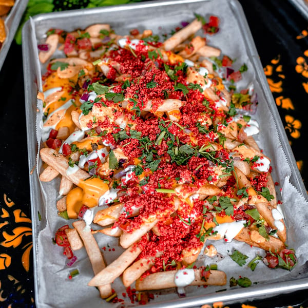 A tray of Talkin' Tacos loaded fries with cheese, red sprinkles, cilantro, and white sauce.