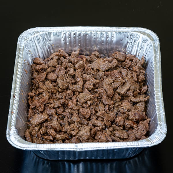 Close-up of seasoned beef chunks in a silver foil tray, ready for Talkin' Tacos.