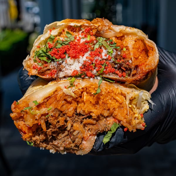 A Talkin' Tacos burrito, cut in half, revealing rice, meat, cheese, and red crunchy toppings.