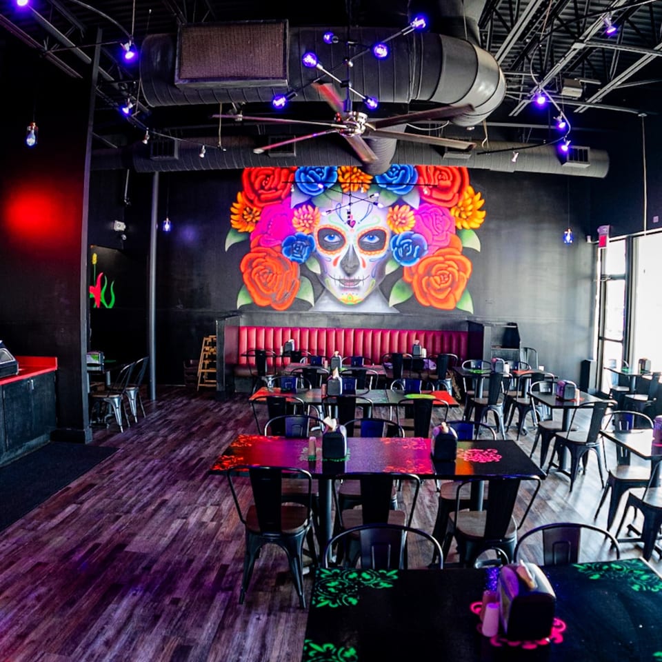 Interior of Talkin' Tacos restaurant with a large colorful sugar skull mural and empty tables.