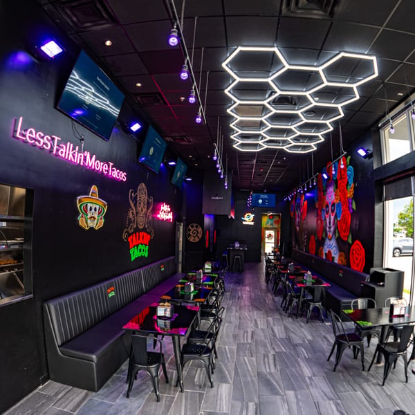 The interior of Talkin' Tacos restaurant, featuring neon signs, dark decor, and vibrant murals.