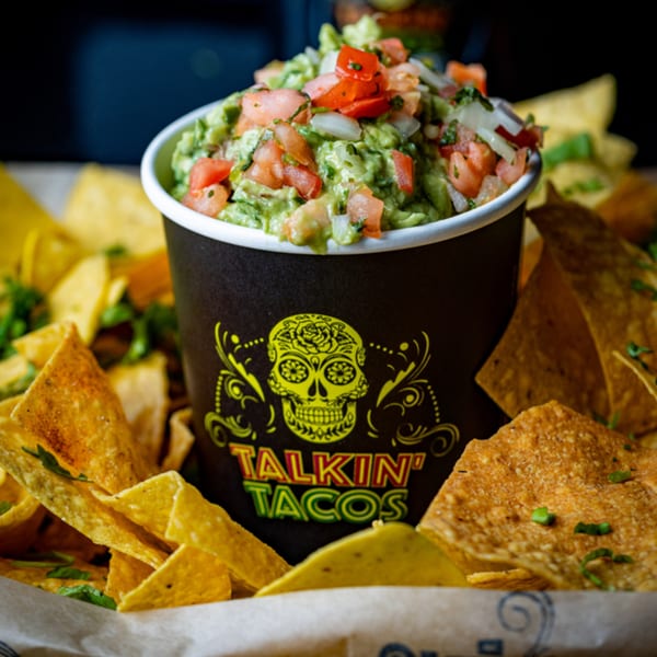 Talkin' Tacos guacamole with diced tomatoes and onions, surrounded by crispy tortilla chips.