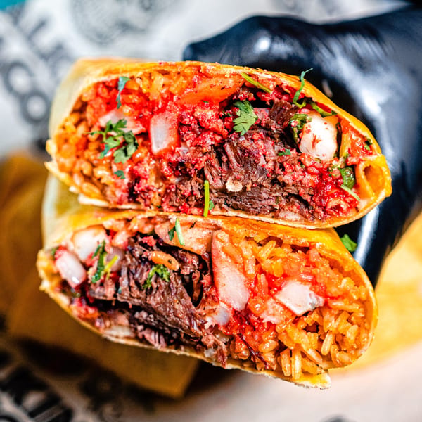 A Talkin' Tacos burrito cut in half, revealing rice, meat, and red sauce.